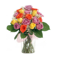 Mixed bouquet of yellow, orange, and purple roses with baby's breath in a clear glass vase