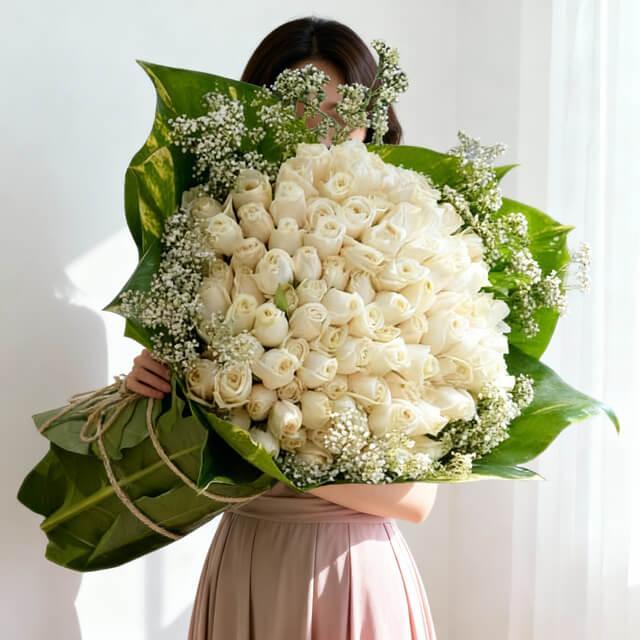 Bouquet of 99 white roses with green leaves and baby's breath, held in bright natural light