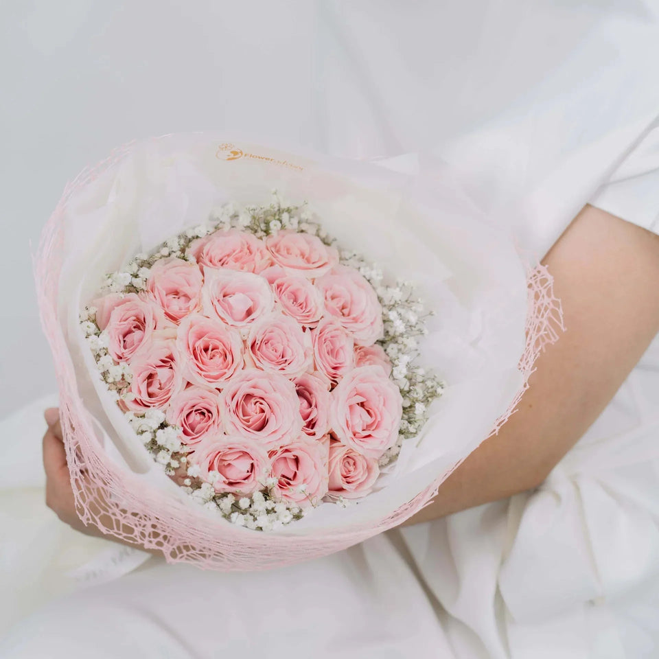 Hand holding bouquet of fresh pink roses and white baby’s breath flowers wrapped in pink net, on white background