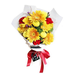 Bouquet of yellow gerbera daisies and red carnations wrapped in white paper with a red ribbon