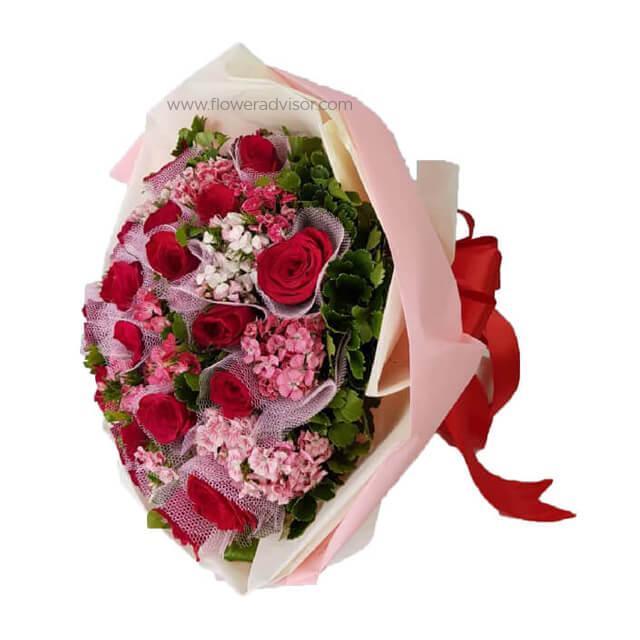 Bouquet of 12 red roses with pink sweet william flowers and greenery, wrapped in pink paper
