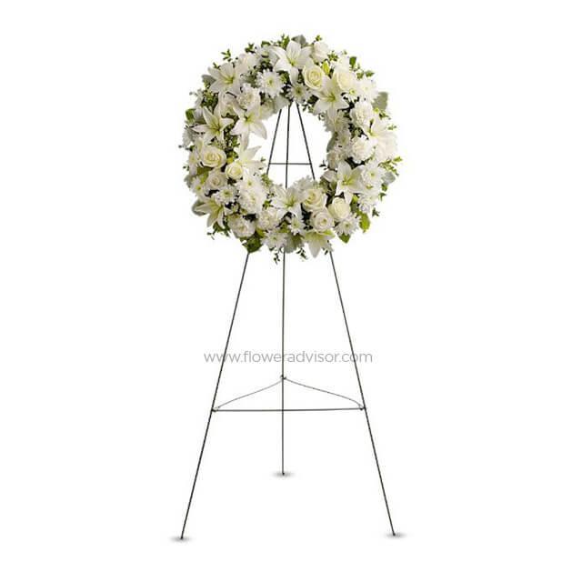 White funeral wreath with lilies and roses on a metal stand, sympathy flower arrangement
