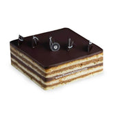 Layered almond biscuit cake topped with chocolate and coffee essence, decorated with chocolate pieces