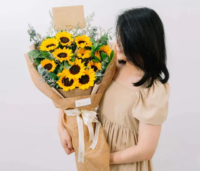 Woman holding large sunflower bouquet wrapped in burlap, perfect for graduation or celebration