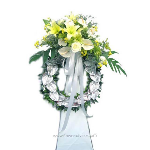 Elegant funeral flower wreath with white and yellow lilies, roses, greenery, and white ribbon by FlowerAdvisor Malaysia