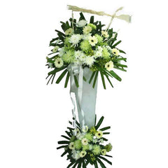 Tall white funeral flower stand with white and pale green chrysanthemums and gerberas, decorated with green leaves