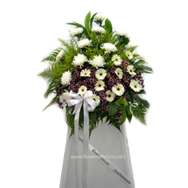 Elegant flower arrangement with white and purple blooms, green leaves, and white ribbon on stand