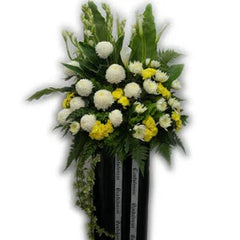 Flower arrangement with white and yellow blooms and green foliage in a black stand, fresh bouquet delivery