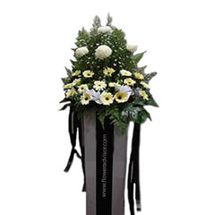 Standing flower arrangement with white and yellow chrysanthemums and daisies, accented by greenery, displayed in a tall box with black ribbons.