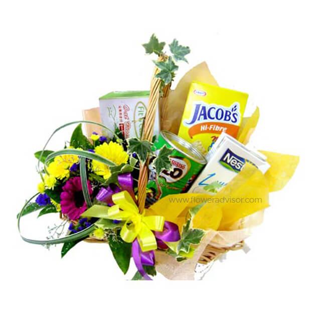 Gift basket with fresh yellow and purple flowers, greenery, and assorted snacks including Jacob's crackers and Nespray milk