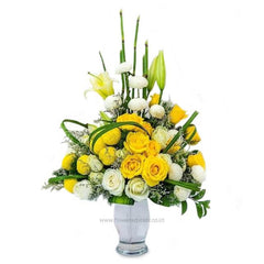 Elegant bouquet of yellow roses, white flowers, and green foliage arranged in a clear glass vase