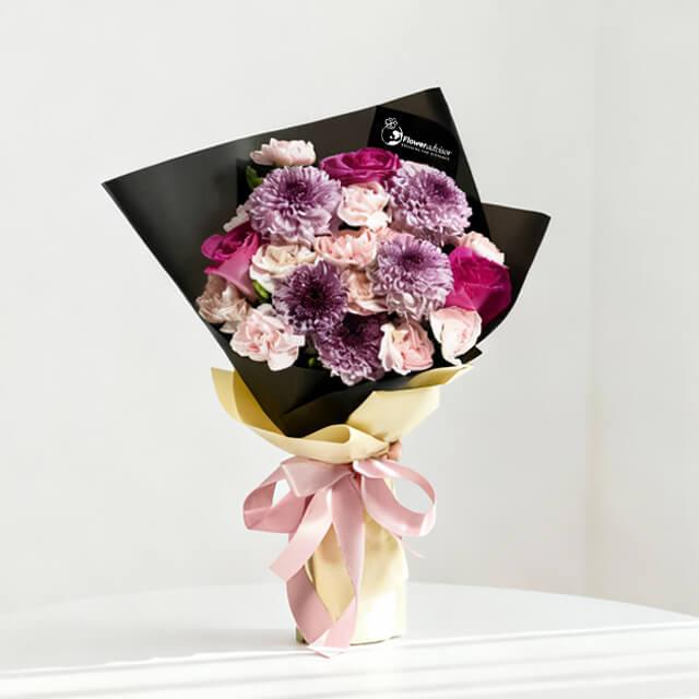 Elegant bouquet of purple chrysanthemums and pink roses wrapped in black and cream paper with pink ribbon