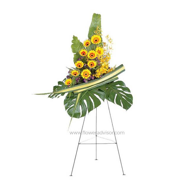 Yellow gerbera and orchid flower arrangement with large green leaves on a stand, fresh floral display