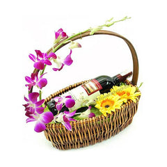 Wicker gift basket with red wine bottle adorned with purple orchids and yellow gerbera daisies, fresh flower delivery