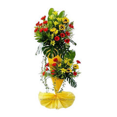 Two-tier flower stand with yellow lilies, sunflowers, red daisies, large green leaves, and yellow wrapping base