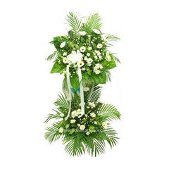Tall symmetrical condolence flower stand with white flowers and lush green tropical leaves