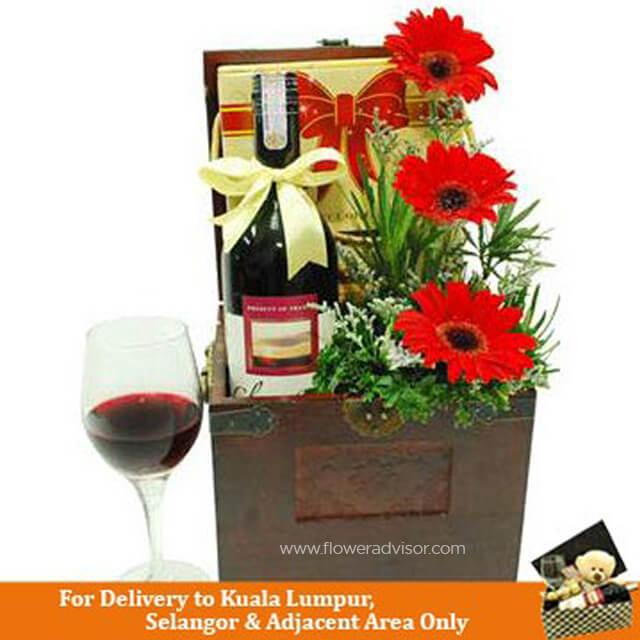Gift box with a bottle of red wine, vibrant red gerbera flowers, green foliage, and a glass of wine, ideal for Kuala Lumpur delivery