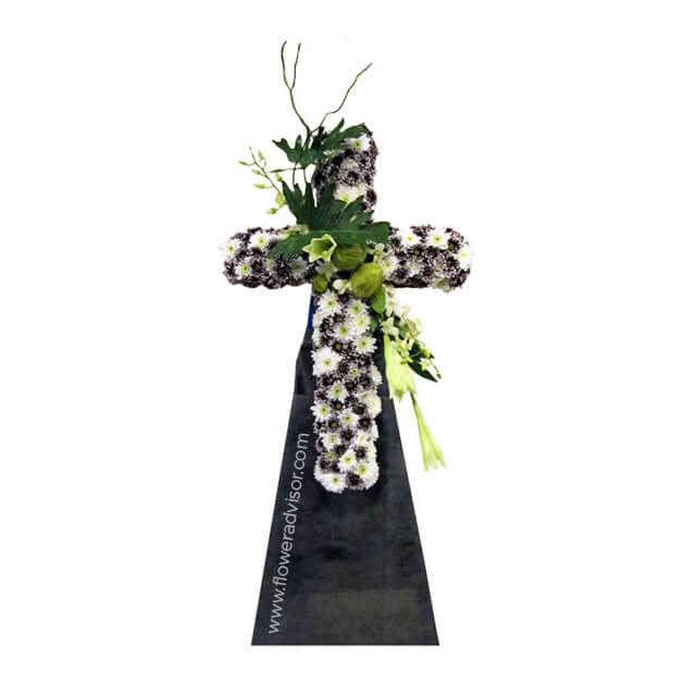 Symmetrical floral cross arrangement with white and purple flowers, green foliage on black stand