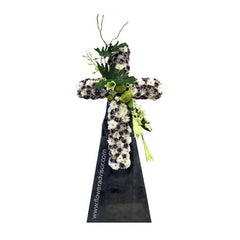 Symmetrical floral cross arrangement with white and purple flowers, green foliage on black stand