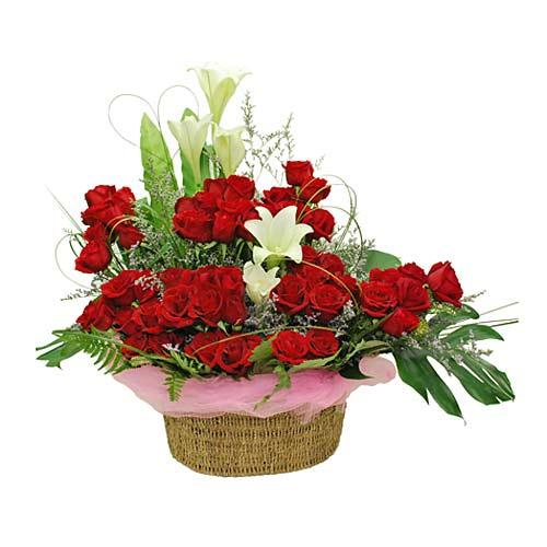 Basket flower arrangement with red roses and white lilies surrounded by green foliage
