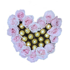 Heart-shaped arrangement of pink roses surrounding Ferrero Rocher chocolates on white background