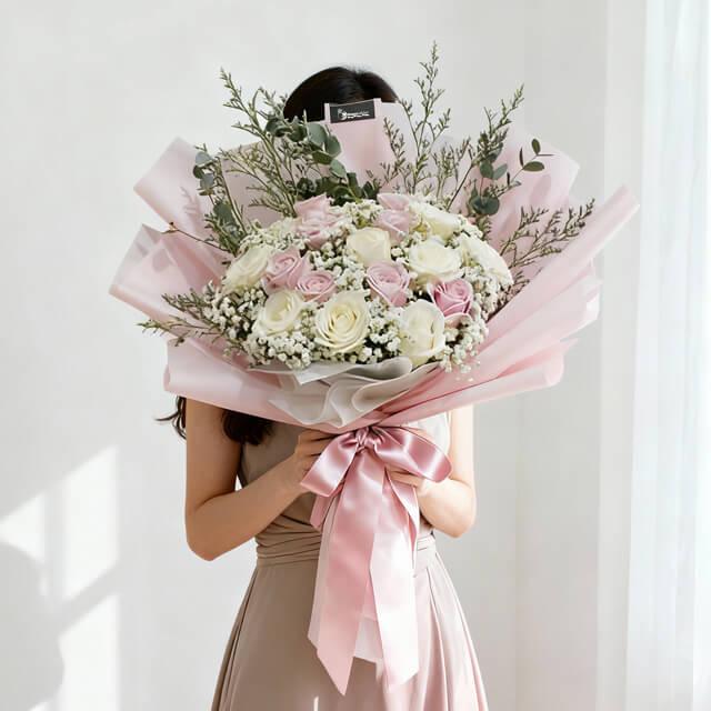 Elegant bouquet of white and pink roses with greenery wrapped in pink paper and ribbon
