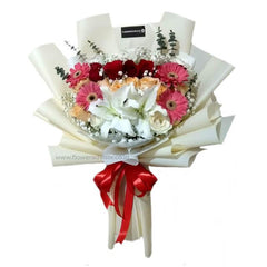 Elegant mixed flower bouquet with white lilies, red roses, pink gerbera daisies, wrapped in cream paper with red ribbon