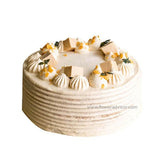 Round cream cake decorated with cream swirls, white chocolate squares, and green leaves on white background