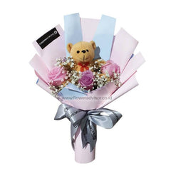 Bouquet of pink and purple roses with baby's breath flowers and a small teddy bear, wrapped in pastel paper with a silver ribbon