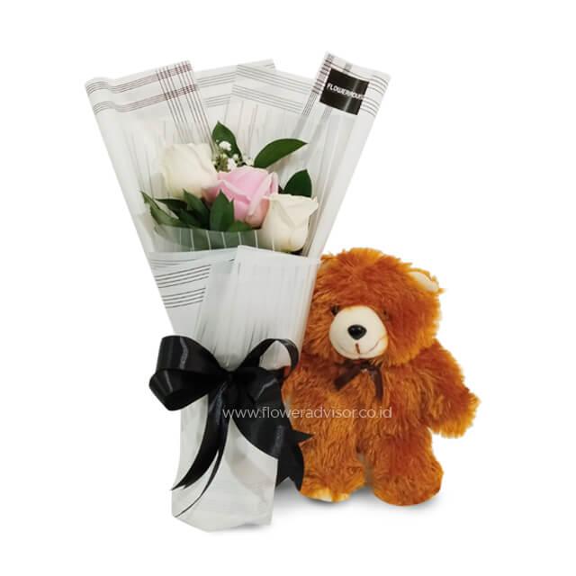 Bouquet of pink and white roses wrapped in striped paper with black ribbon next to a small brown teddy bear
