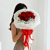 Woman holding a large bouquet of red roses and white baby's breath, wrapped in white paper with a red ribbon