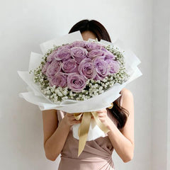 Woman holding large bouquet of fresh lavender roses and white baby's breath wrapped in white paper with gold ribbon