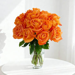 Fresh bouquet of vibrant orange roses in clear glass vase on white table with soft natural light