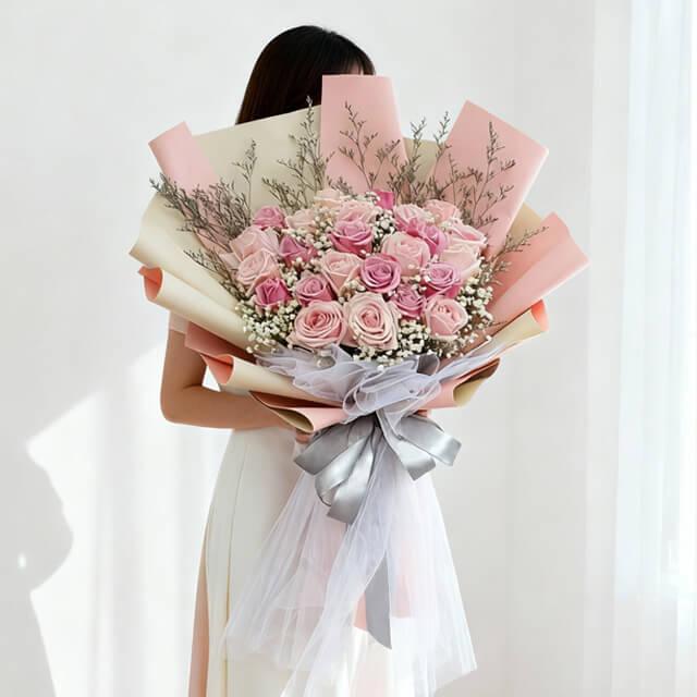 Woman holding large bouquet of pink and light pink roses wrapped in pastel paper with silver ribbon