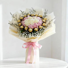 Elegant bouquet with white and pink roses, Ferrero Rocher chocolates, baby's breath, and greenery, wrapped in cream paper with a pink ribbon