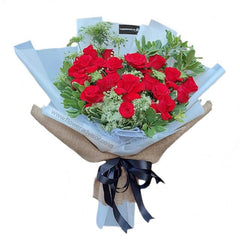 Bouquet of fresh red roses with green foliage wrapped in blue and burlap paper, tied with black ribbon