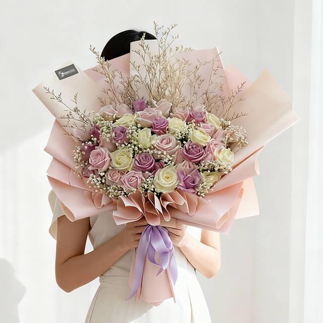 Large bouquet of pink and white roses with baby's breath and dried twigs wrapped in pink paper with lavender ribbon