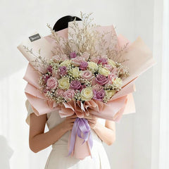 Large bouquet of pink and white roses with baby's breath and dried twigs wrapped in pink paper with lavender ribbon