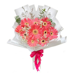Bright pink gerbera daisy bouquet with white baby's breath and green leaves wrapped in white paper with pink ribbon