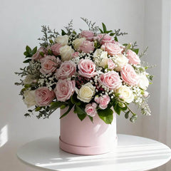 Elegant bouquet of pink and white roses with greenery in a round pink vase on white table