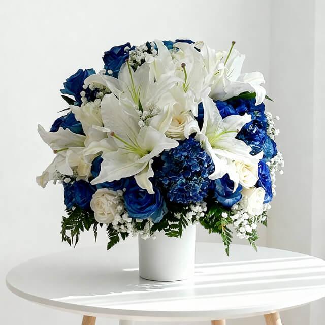 Elegant bouquet of white lilies, blue and white roses, and baby's breath in white vase on table