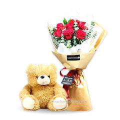Bouquet of red roses wrapped in brown paper with a red ribbon beside a light brown teddy bear
