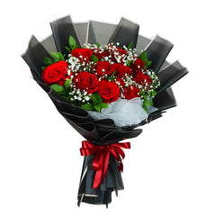 Elegant bouquet of red roses with white baby's breath and green leaves wrapped in black paper with red ribbon