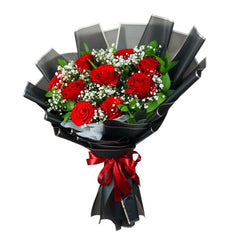 Bouquet of fresh red roses with white baby's breath and green leaves wrapped in black matte paper and tied with red satin ribbon