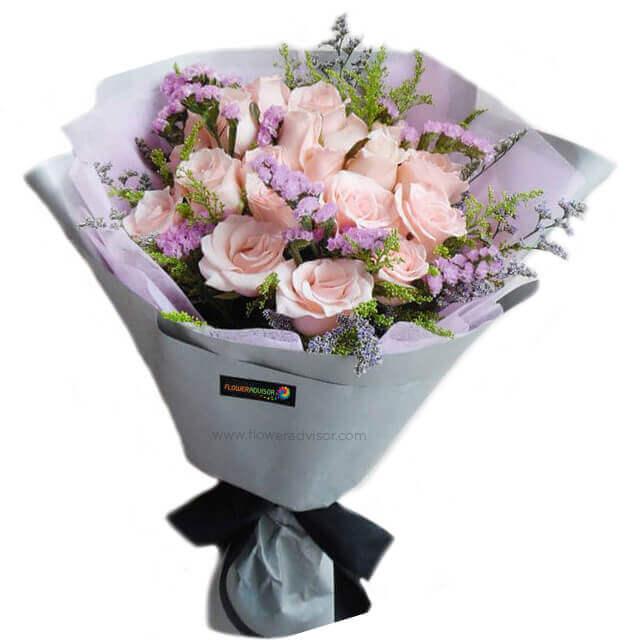 Elegant bouquet of pale pink roses and purple filler flowers wrapped in lavender paper with black ribbon