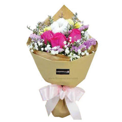Bouquet of pink roses, white flowers, and purple accents wrapped in brown paper with pink ribbon bow