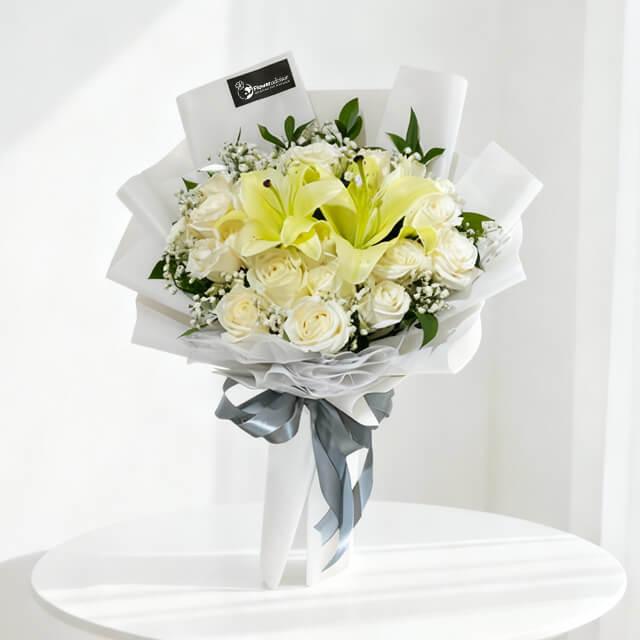 Elegant bouquet of white roses and yellow lilies wrapped in white paper with gray ribbon on white table