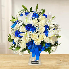 Elegant bouquet of blue and white roses with white lilies and greenery in clear vase