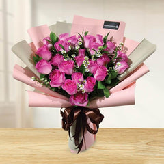 Bouquet of fresh pink roses and white daisies wrapped in pink paper with brown ribbon on wooden table