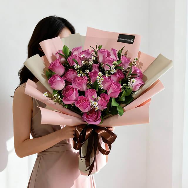 Woman holding large bouquet of pink roses wrapped in pink and beige paper with greenery and small white flowers
